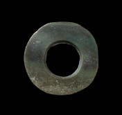 Jade bi 
Acc. no. 2017.0067 
Made from pale green jade with black patches, the bi had an irregular outer perimeter, showing that it had been polished to get rounder from a square shape. The bore hole was drilled from one side.