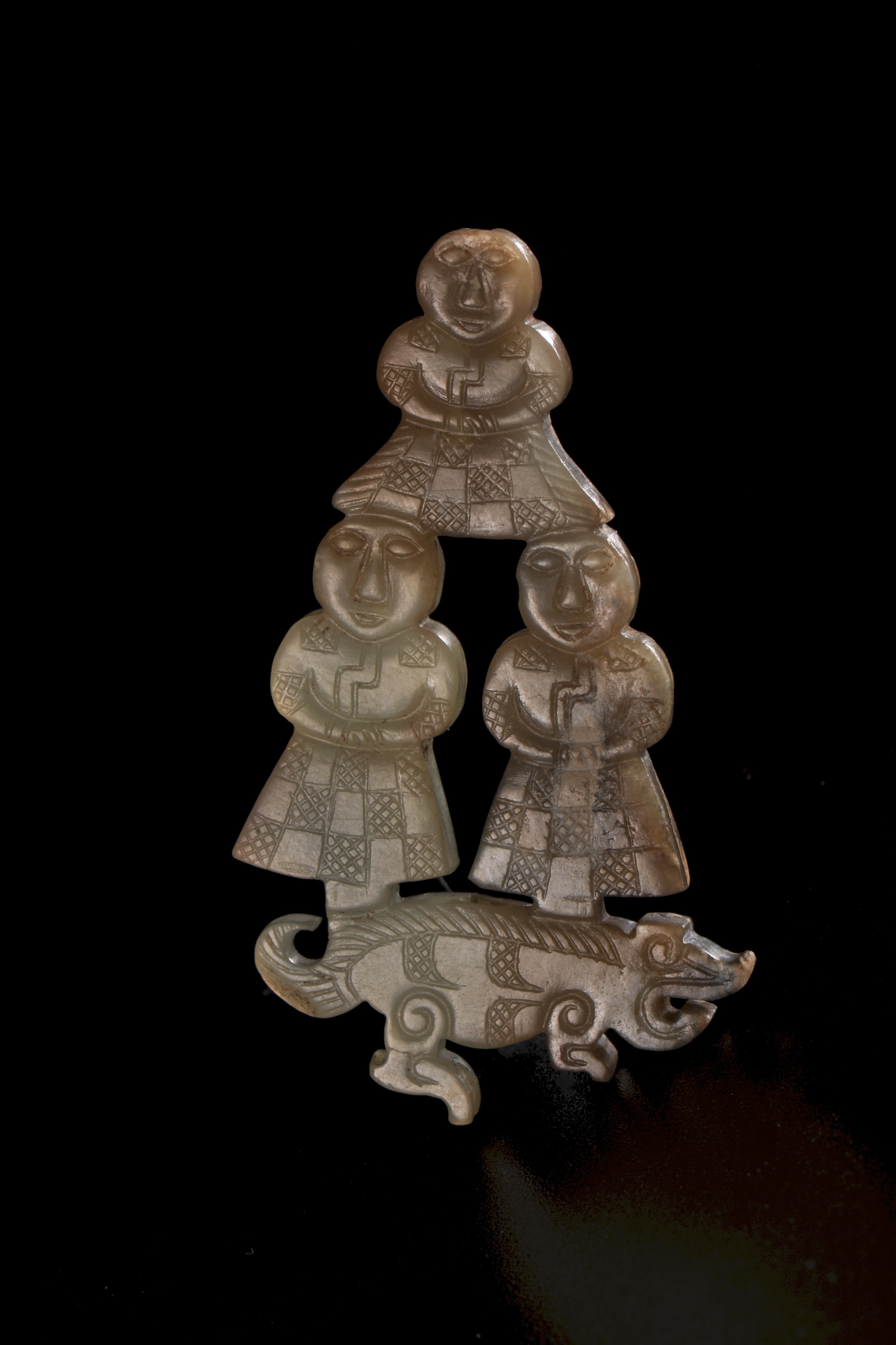 Jade pendant in the shape of three men standing on a hog
Warring States Period
L: 5.1 W: 3 Th: 0.4 cm
Recovered from tomb no.2 at Jiuliandun, Zaoyang, Hubei province in 2002
Hubei Provincial Museum

Pendants with man holding their hands standing on top of a dragon’s tail or holding one dragon in each hand were recovered from Chu tombs in the early to mid-Warring States period, which is analogous to this jade. The characters depicted on these jades could be god, witch or wizard. The meaning was that man could communicate with the spirits through animals like dragon and hog. This was a display of the worshiping of animals and spirits. The long robes wore by these gods were engraved with rectangular net pattern checkered with rectangular plain boxes, which was the style of jade engravings from Zhongshan State founded by the Di people located in northwestern China.