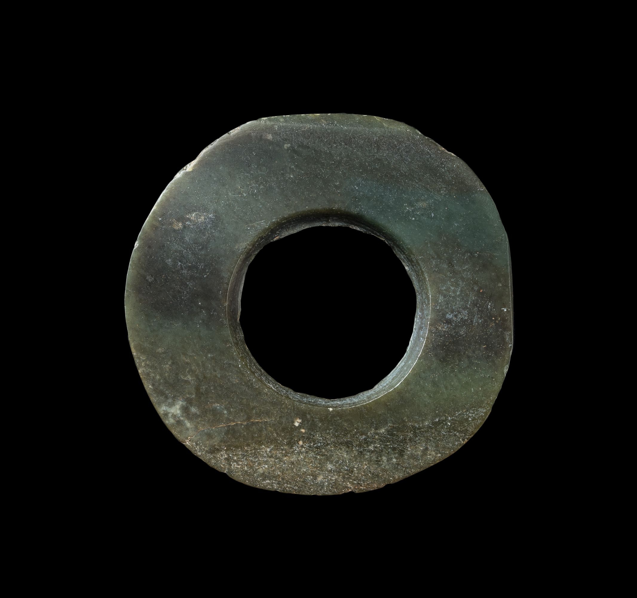 Jade bi 
Acc. no. 2017.0067 
Made from pale green jade with black patches, the bi had an irregular outer perimeter, showing that it had been polished to get rounder from a square shape. The bore hole was drilled from one side.